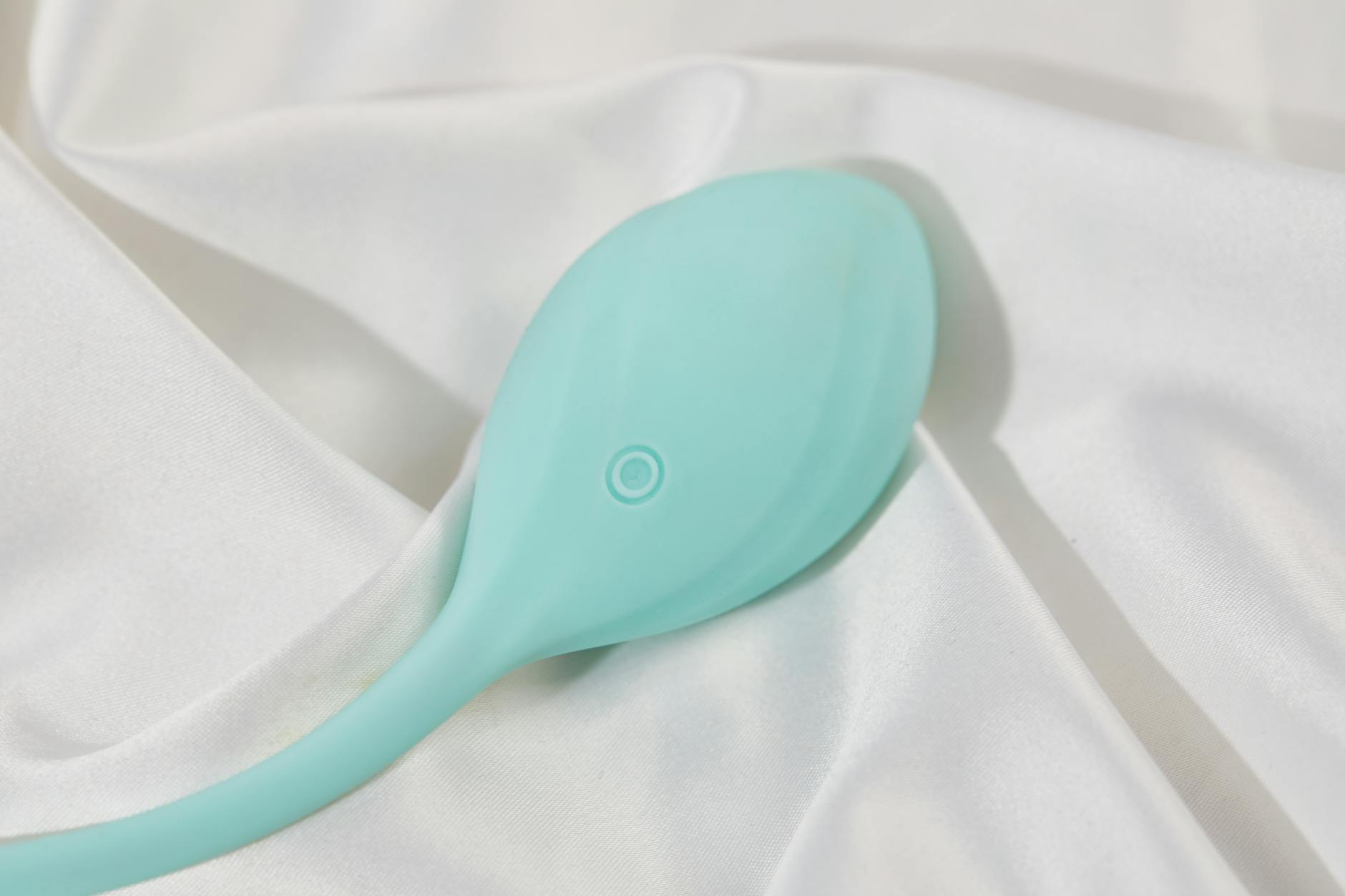 A teal clitoral vibrator on white silk fabric, symbol of modern sexual confidence