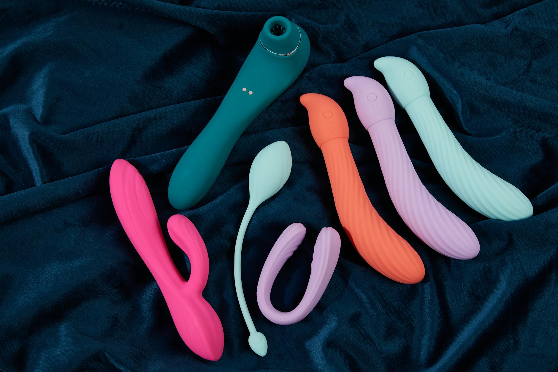Hand holding a modern clitoral vibrator against a minimalist purple background