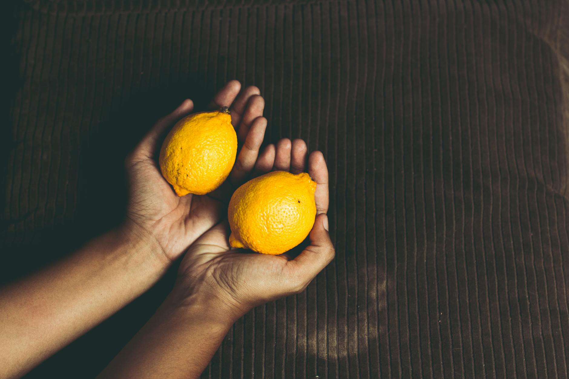 Two fresh lemons held in cupped hands, symbolizing the cyclical rhythm of feminine pleasure.