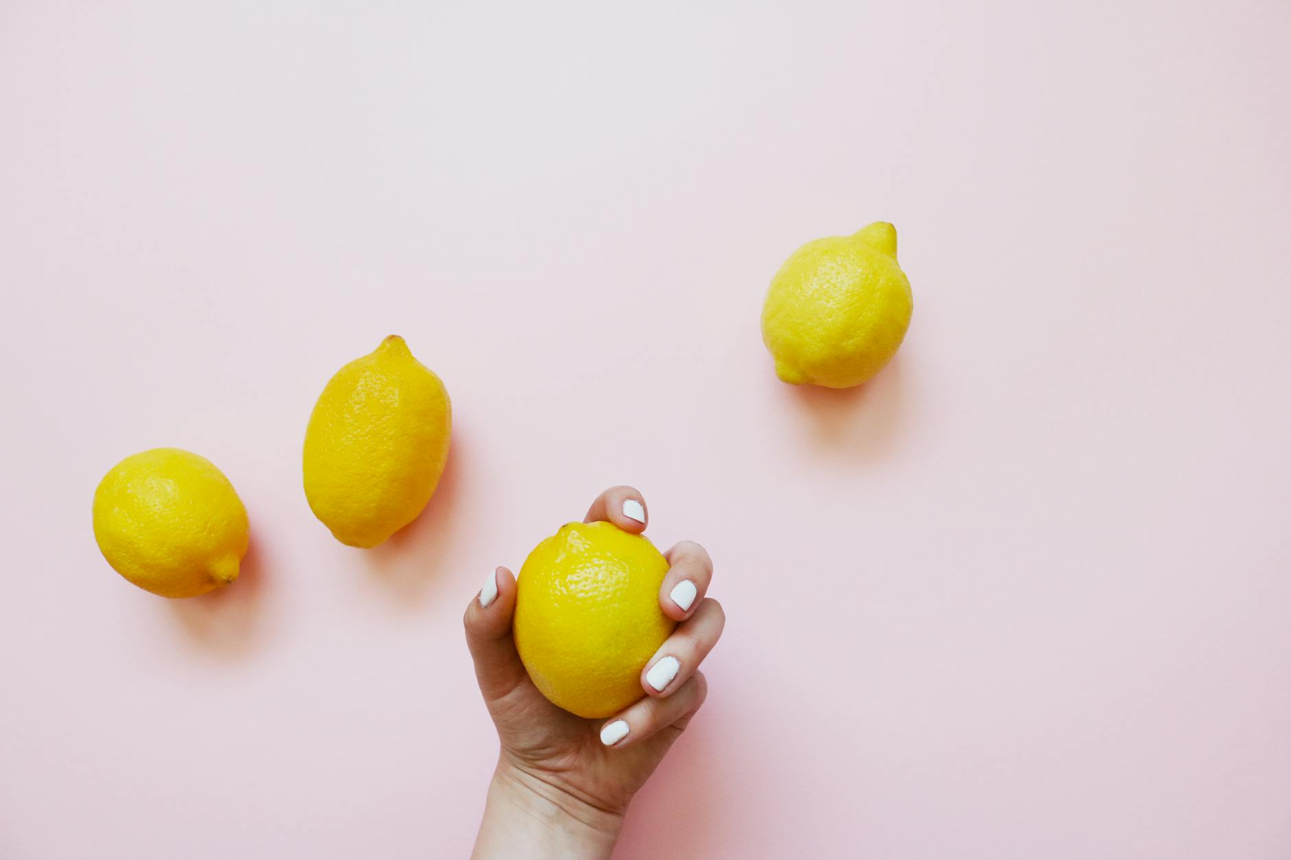 A hand holding fresh lemons on soft pink background symbolizing natural pleasure and wellness
