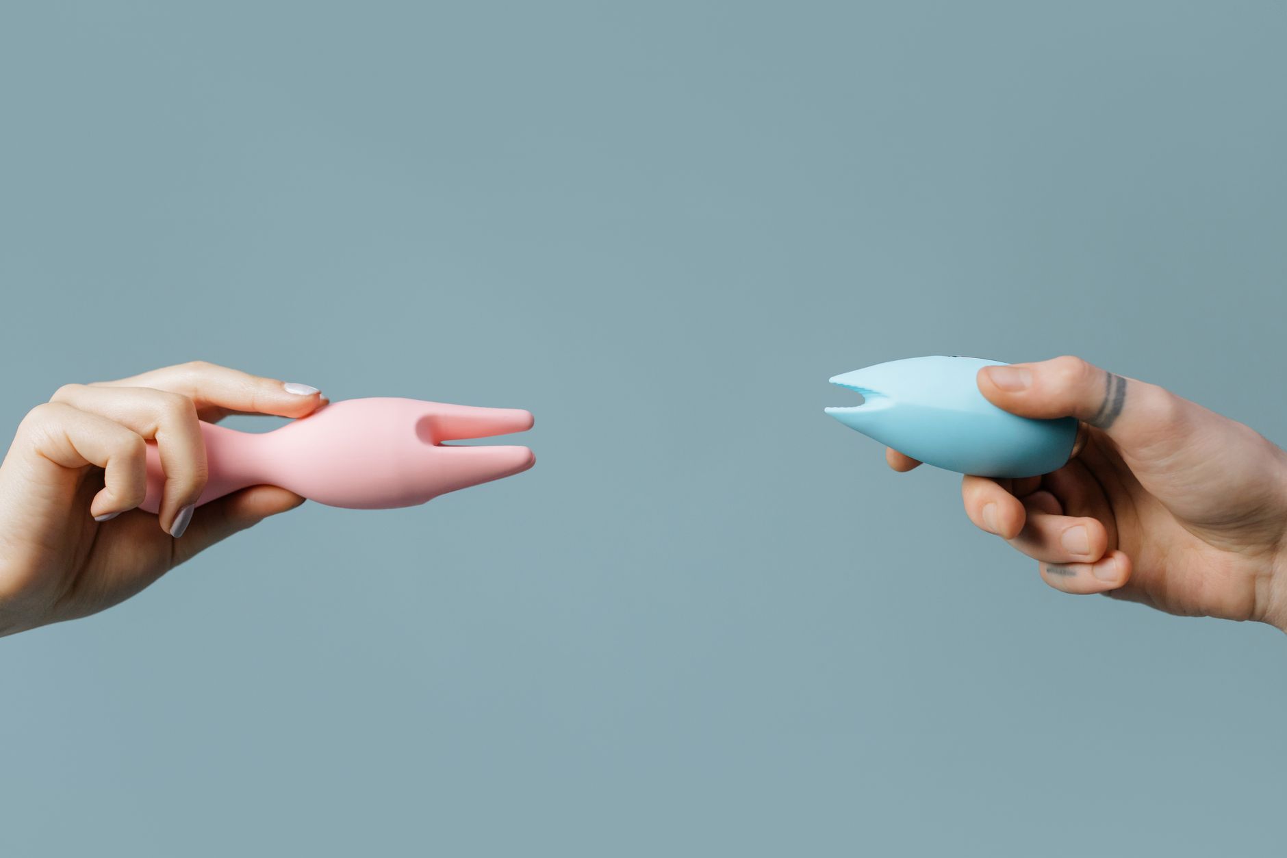 Two hands holding pink and blue lemon clitoral vibrators against a pastel background, symbolizing self-care and personal pleasure.