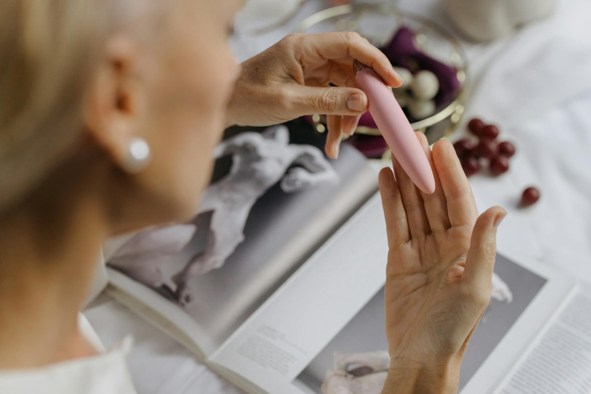 Close-up of a woman holding a pink vibrator with art books nearby, emphasizing personal wellness and intimate self-care