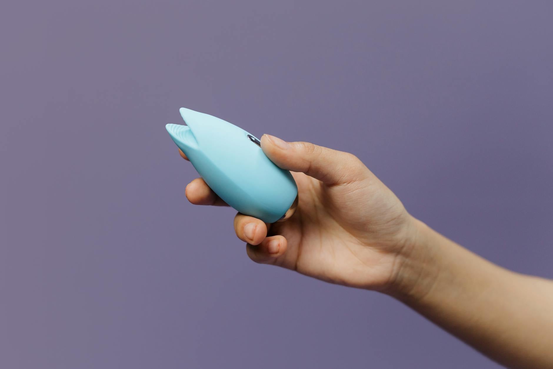 A blue silicone lemon clitoral vibrator held confidently in hand against a purple background