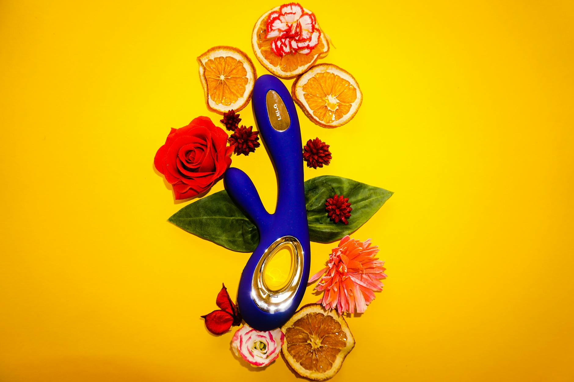A yellow lemon vibrator surrounded by flowers and citrus on a bright yellow background
