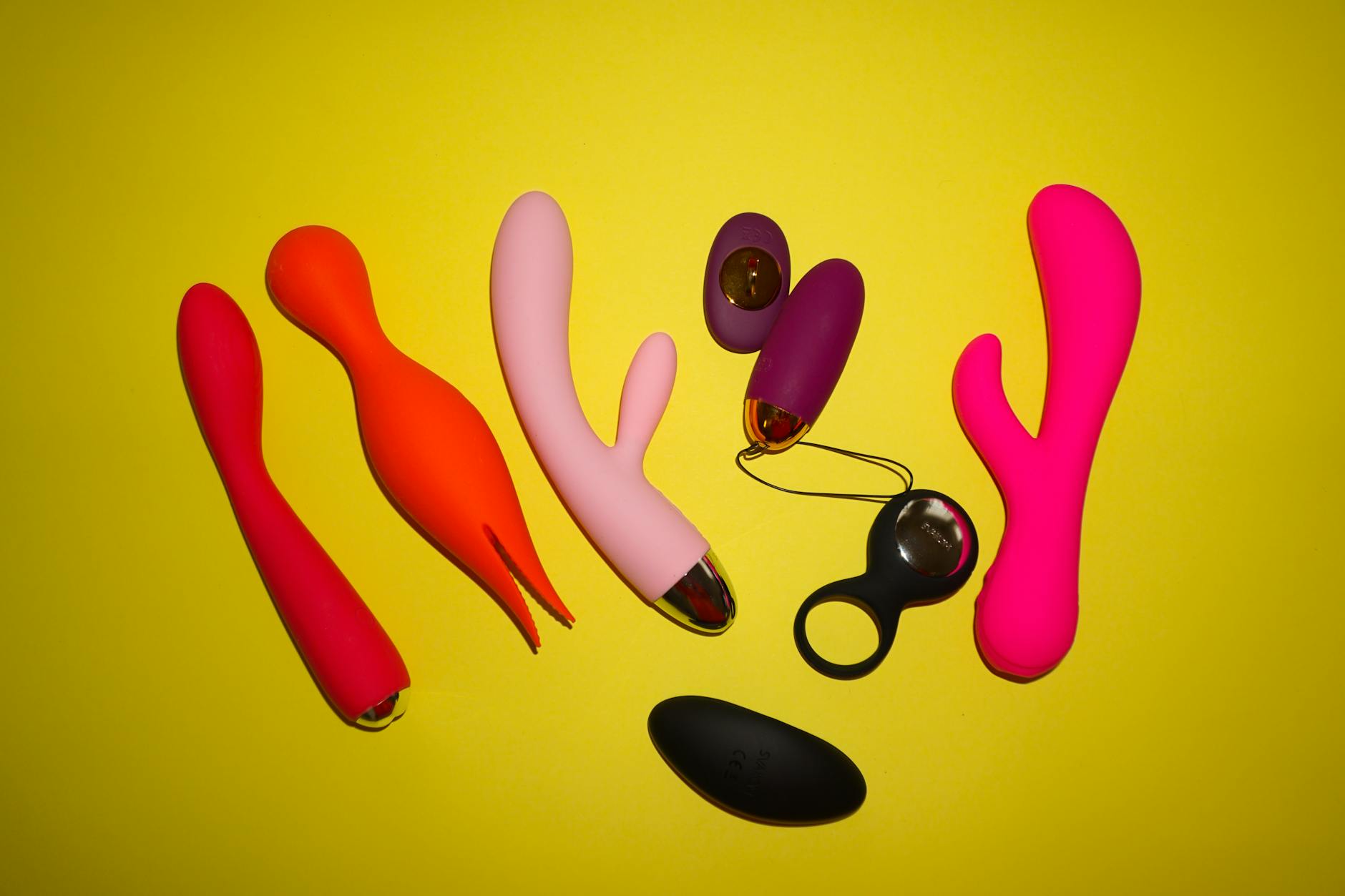 Colorful silicone vibrators on a bright yellow background, representing modern intimacy tools