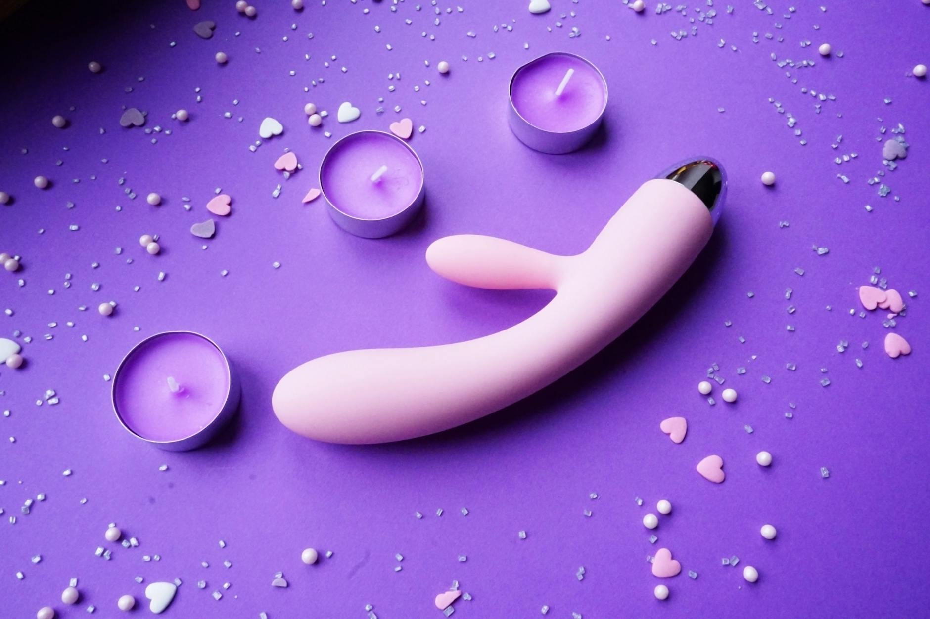 Pink lemon vibrator on a purple background with heart confetti and candles for a romantic vibe.